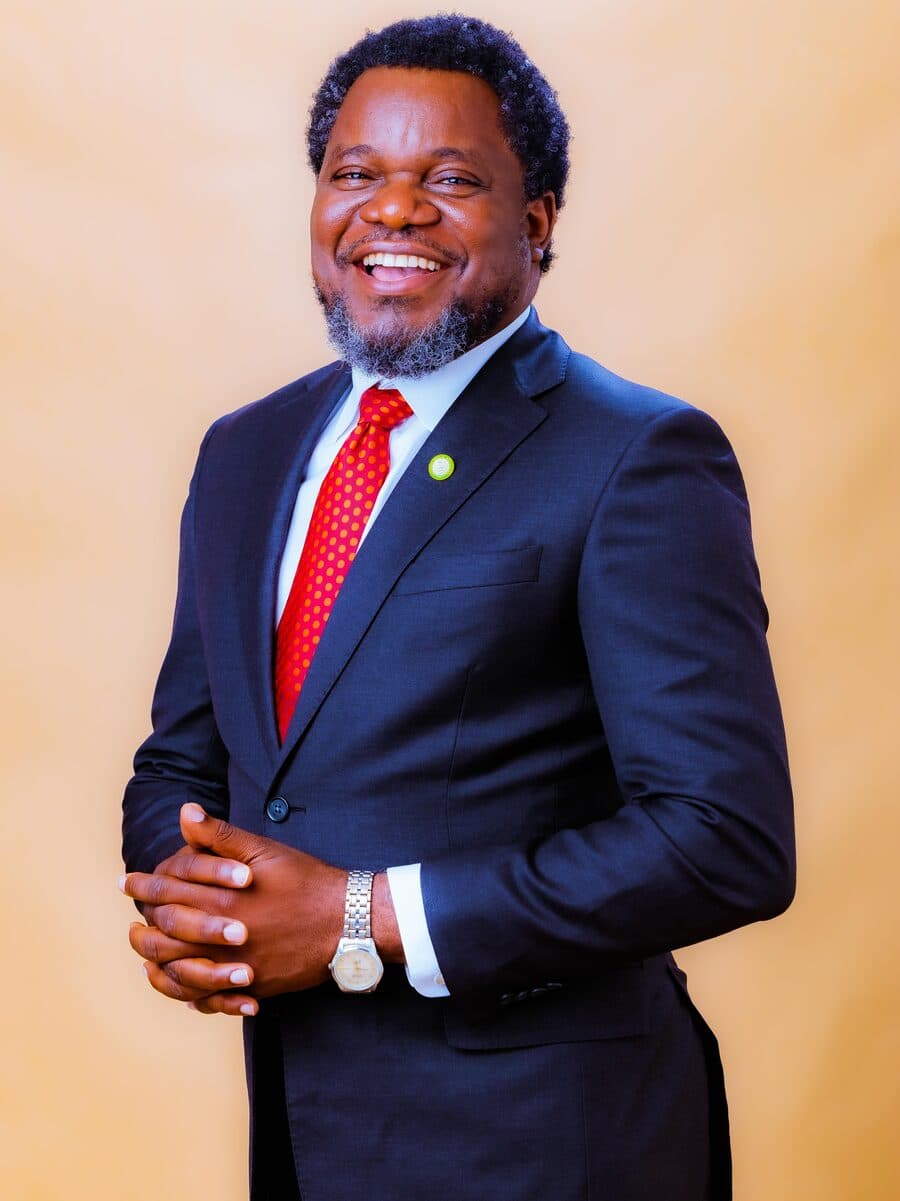 Dr. Olarewaju smiling warmly in a navy suit and red tie